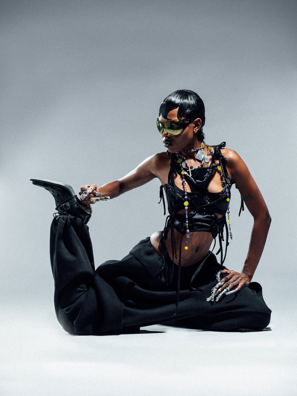 Person wearing a black outfit with intricate jewelry on a gray background