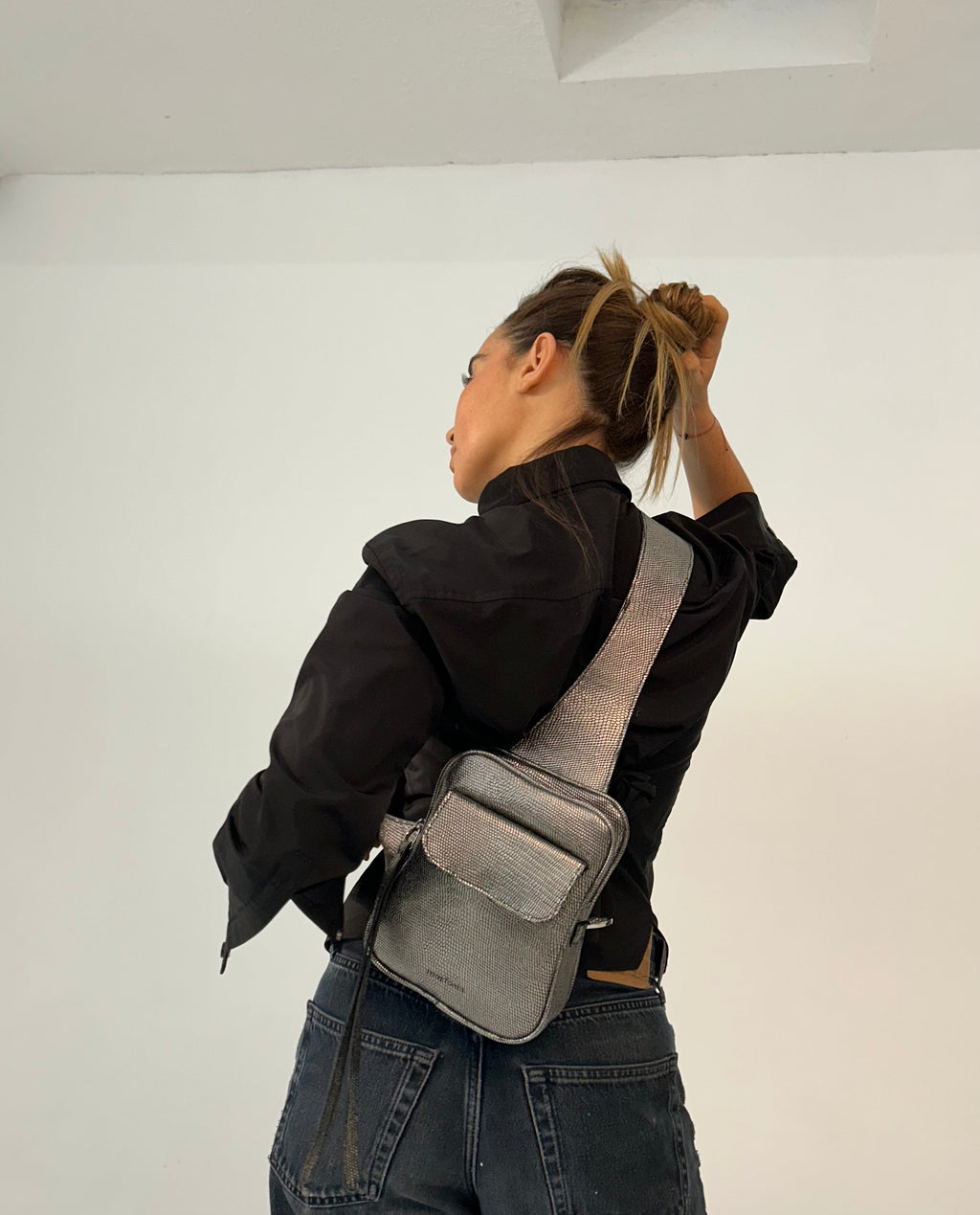 Person wearing a black jacket and gray crossbody bag against a white background