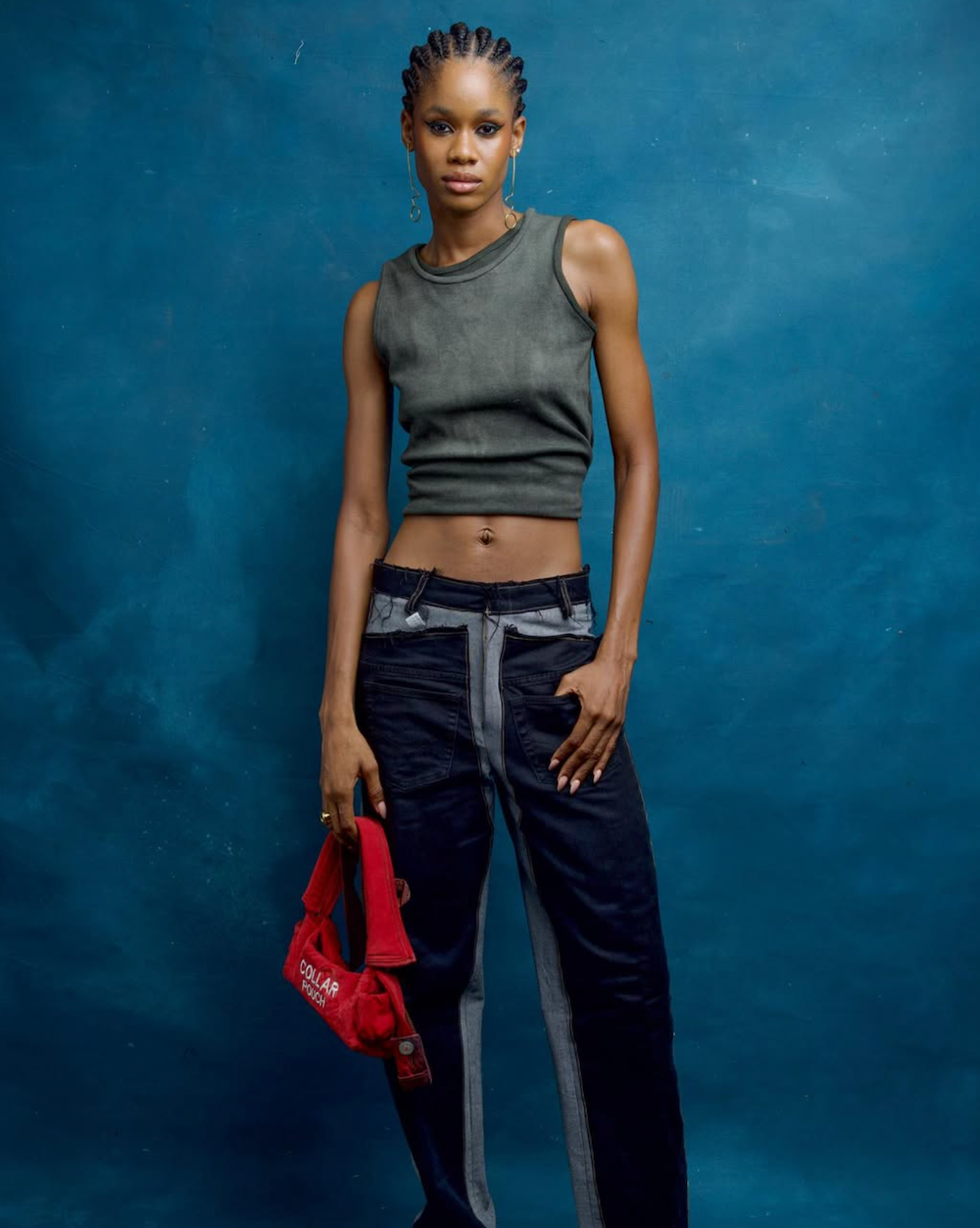 Model wearing a gray sleeveless top and dark pants against a blue background